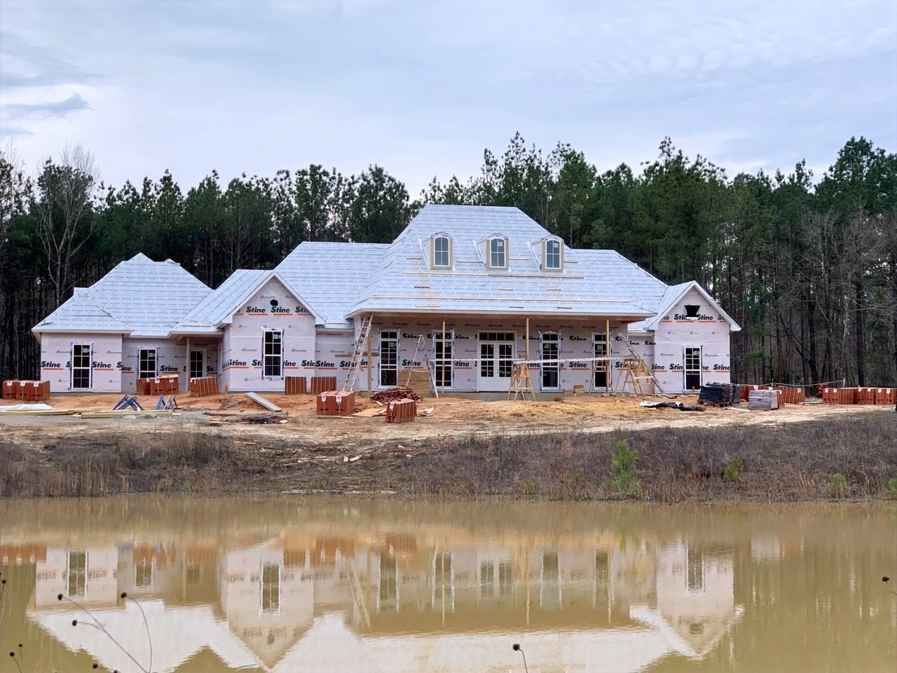 The finished Thomas Bolton residence, a white custom home mirrored in a still pond in Pineville, Louisiana