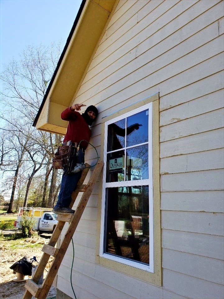 A Mike Carson Construction carpenter installing hard board siding from a ladder